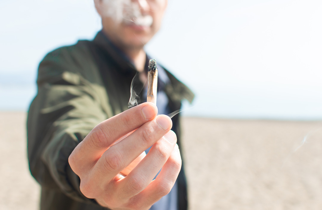 potography introduce yourself forum cover photo - man holding burning lit joint on beach with smoke and blurred background