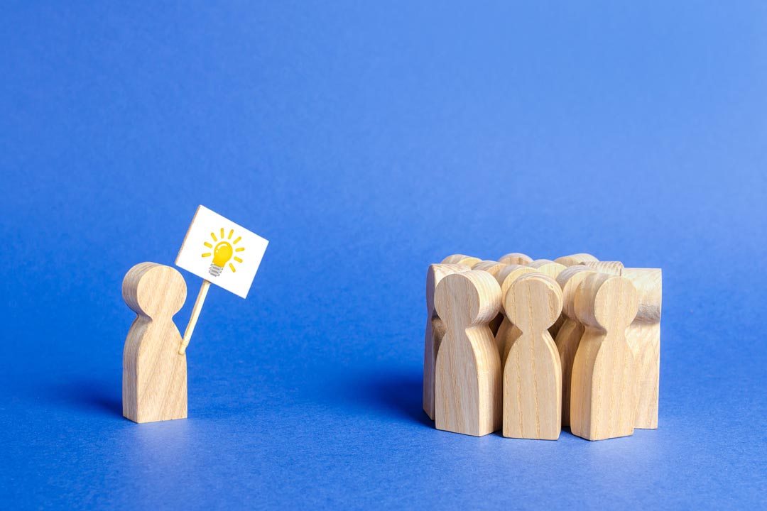 community-suggestions-and-feedback-1-wooden figures in group with another separate from group holding sign with lightbulb icon AdobeStock_281251653